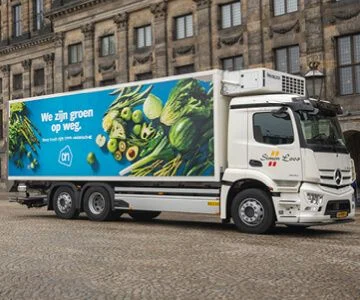 Albert Heijn transport truck delivering groceries to a city supermarket, utilizing Simacan's Control Tower for real-time tracking and efficient shop replenishment